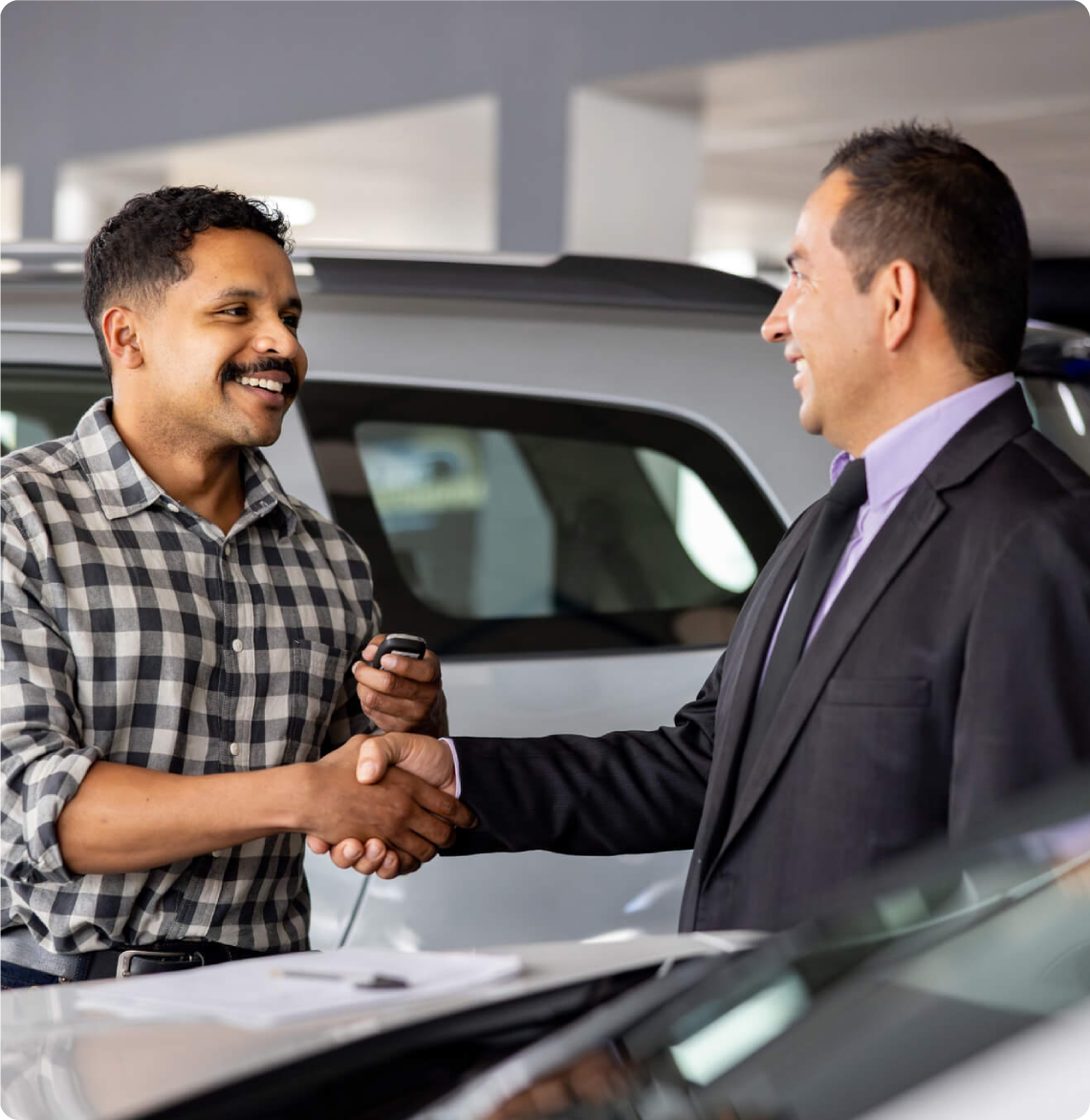 Two men shaking hands at car dealership.